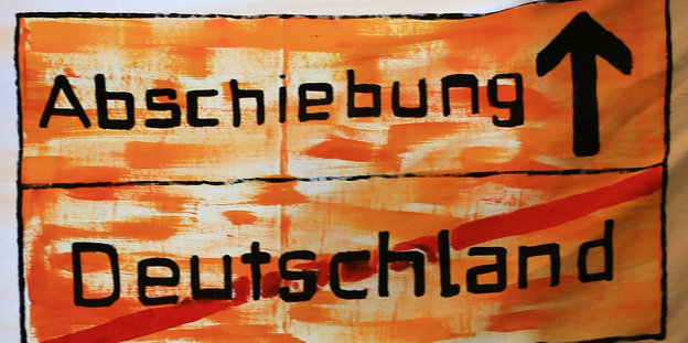 Auf einem gemalten Schild stehht das Wort Abschiebung und daneben ein Pfeil nach oben. Darunter steht das Wort Deutschland. Es ist durchgestrichen
