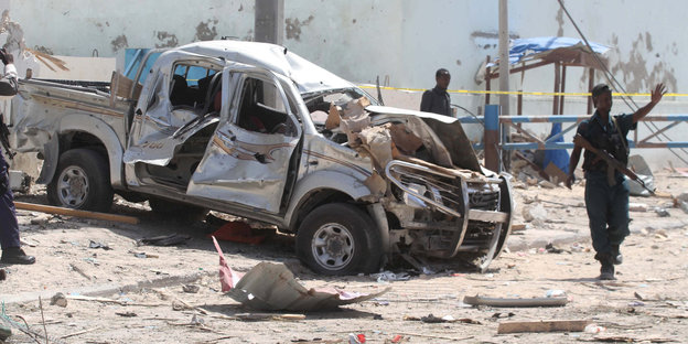 Ein somalischer Polizist steht vor einem ausgebombten Autowrack inmitten von Trümmern