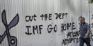 Ein Mann läuft an einer Mauer vorbei auf der "IMF go home" steht