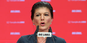 Die Linke Ko-Fraktionsvorsitzende Sahra Wagenknecht an einem Mikrofon, vor ihrem Mund befindet siche in Schild mit der Aufschrift "Die Linke"