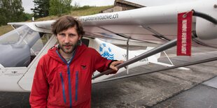 Ein Mann in roter Windjacke steht vor einem Kleinflugzeug