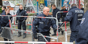 Polizisten tragen Absperrgitter vor einem bemalten und mit Plakaten beklebten Haus