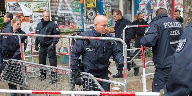Polizisten tragen Absperrgitter vor einem bemalten und mit Plakaten beklebten Haus