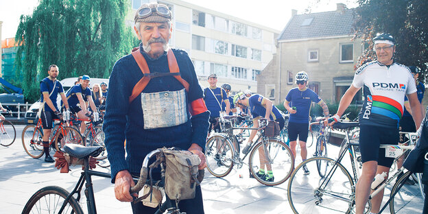 Ein älterer Mann mit Retro-Fahrrad, dahinter weitere Radsportler Ein älterer Mann mit Retro-Fahrrad, dahinter weitere Radsportler