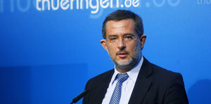 Der Verfassungsschutz-Beamte Stephan J. Kramer steht vor einer blauen Wand, auf der thueringen.de steht