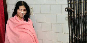 Eine Frau, Irom Chanu Sharmila, eingewickelt in eine rosa Decke. In ihrer Nase steckt ein Ernährungsschlauch