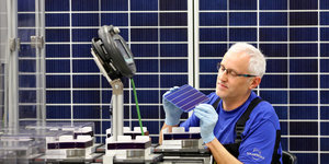 Ein Mann im Blaumann arbeitet in einer Fabrik für Photovoltaikanlagen