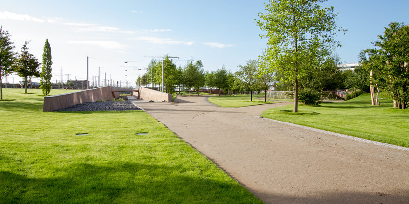 Eine flache grüne Parklandschaft, durchzogen von einem geraden Weg