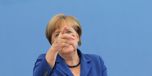 Angela Merkel vor einer blauen Wand, sie zeigt nach vorne