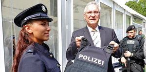 Joachim Herrmann hält eine schutzsichere Weste, daneben steht eine Polizistin