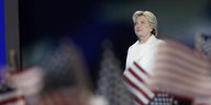 Hillary Clinton auf einer Bühne, im Vordergrund US-Fähnchen