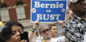 Eine junge Frau hält ein Schild mit der Aufschrift "Bernie or Bust" in die Luft