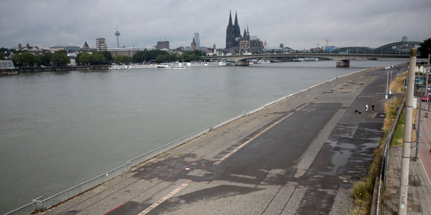 Asphaltierte Fläche, dahinter ein Fluss, dahinter die Skyline von Köln