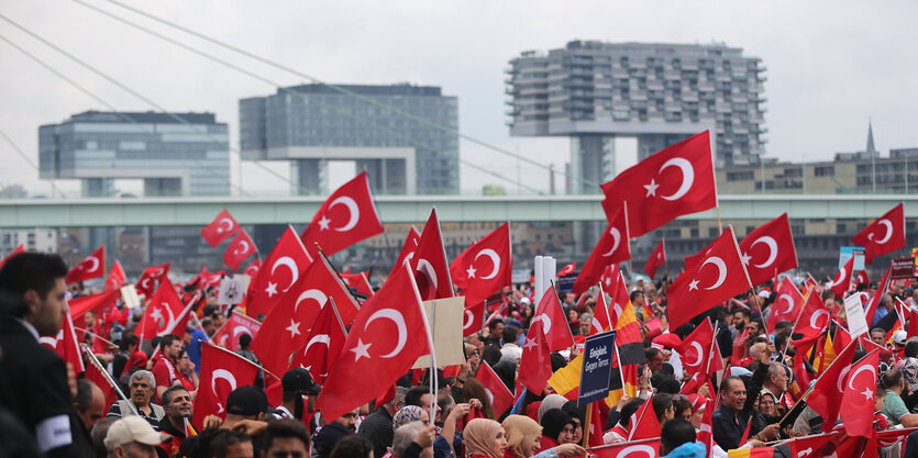 Viele Menschen mit Türkei-Fahnen vor modernen Gebäuden (die in Köln am Rhein stehen)