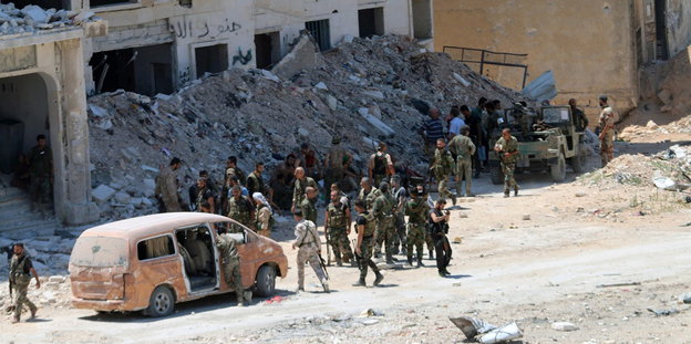 Syrische Regierungssoldaten vor einem zerstörten Gebäude neben einem Kleinbus