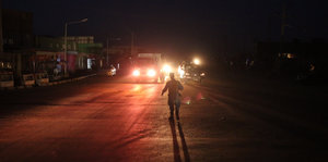 Nacht-Aufnahme, Mann auf einer Straße, der von hinten von Scheinwerfern angestrahlt wird