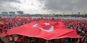 Menschenmenge am Ufer eines Flusses mit großer Türkei-Fahne