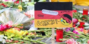 Eine Deutschlandfahne mit der Aufschrift "Warum" zwischen Blumen und Kerzen