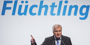 Seehofer vor einer Wand, auf der "Flüchtling" steht