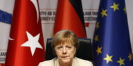 Merkel sitzt vor einer Türkei-, einer Deutschland- und einer EU-Flagge