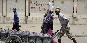 Ein Mann schiebt einen Karren vor einer Wand mit der Aufschrift: "Kill Boko Haram not Shia"