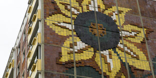 Eine Hausfassade mit einem Sonnenblumenmosaik. Es ist das Sonnenblumenhaus in Rostock-Lichtenhagen