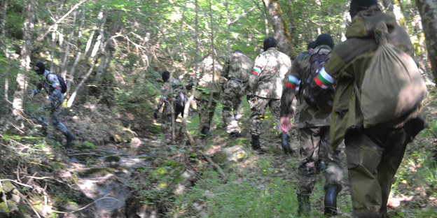 Eine Gruppe Männer in Flecktarn-Uniformen läuft in einer Reihe durch einen Wald