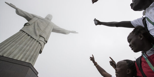Drei Menschen strecken ihre Hände nach der Jesus-Statue von Rio de Janeiro aus