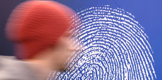 Ein Mann mit roter Mütze, im Hintergrund ein überdimensionierter Fingerabdruck