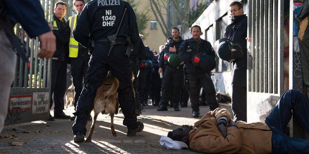Ein Mann liegt am 1. Mai vor dem Tor der von Flüchtlingen besetzten Gerhart-Hauptmann-Schule in Kreuzberg, während Polizisten das Gelände sichern.
