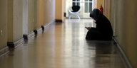 Frau mit Smartphone sitzt in einem langen Korridor