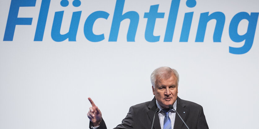 Horst Seehofer steht unter übergroßen Lettern, die das Wort Flüchtling bilden