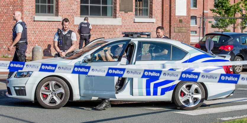 Ein Polizeiauto und mehrere Polizisten hinter einer Absperrung