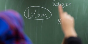 Mädchen mit Kopftuch meldet sich, vor ihr eine Tafel, auf der Islam steht