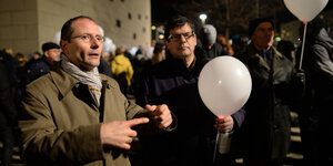 Sachsens Innenminister bei Pegida Demo. Rechts neben ihm hält ein Mann ein Luftballon. Es ist abend.