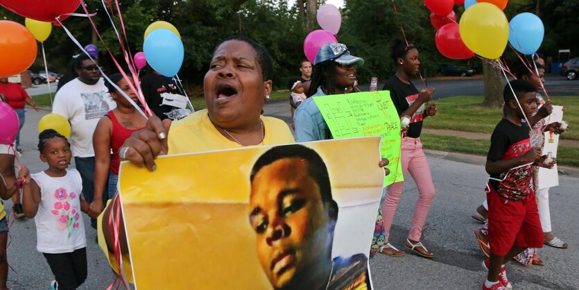 Eine Frau hält ein Plakat mit einem Foto von Michael Brown, mehre Erwachsene und Kinder tragen bunte Luftballons