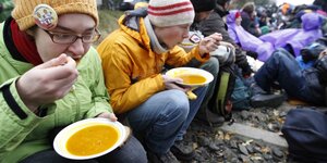 Menschen sitzen auf Schienen und essen Suppe