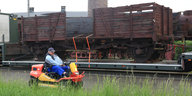 Ein Mann auf einem Rasenmäher fährt an einem Eisenbahnwaggon vorbei