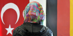 Eine Person mit Kopftuch vor der deutschen und türkischen Flagge