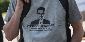 ein Mann, auf dessen Hemd „#Terrorthomas“ unter einem Bild de Maizières steht