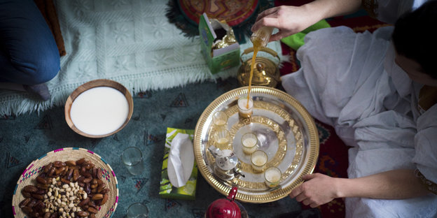 Eine Schale mit Datteln und Nüssen und ein Mann, der Gläser auf einem Tablett mit Tee füllt