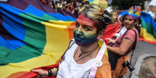Eine Frau mit Regenbogenbemalung im Gesicht hält eine Regenbogenflagge