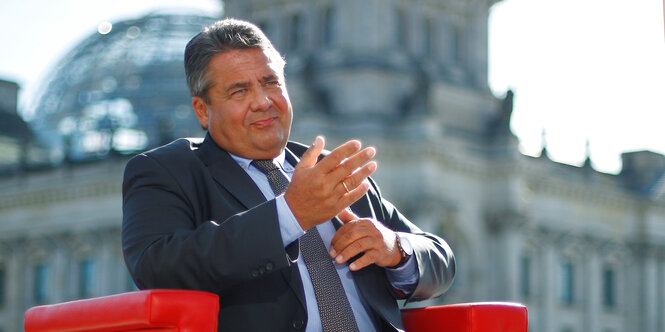 Sigmar Gabriel sitzt auf einem roten Sessel, im Hintergrund ist die Kuppel des Reichstagsgebäudes zu sehen