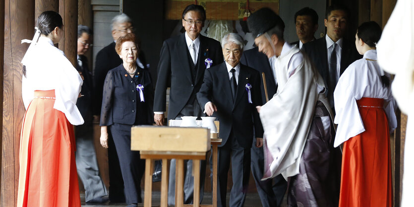 Eine Gruppe japanischer Männer und Frauen stehen vor einem kleinen Tisch