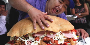 ein Mann drückt mit seiner Hand auf einen gigantischen Sandwich