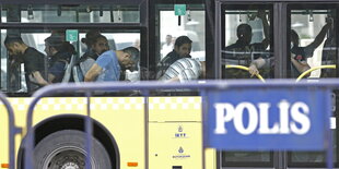 Ein Bus in dem Menschen mit scheinbar am Rücken gefesselten Händen sitzen