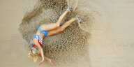 Eine athletische Frau mit blondem Zopf ist nach einem Weitsprung im Sand gelandet