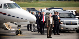 Trump steht neben Begleitern auf einem Flugfeld und winkt