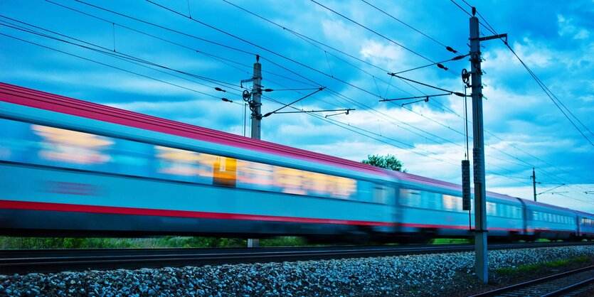 Ein Zug mit hellerleuchteten Fenstern fährt durch die Morgen- oder Abenddämmerung