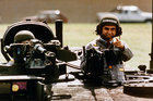 Mike Dukakis in Soldatenoutfit guckt aus einem Panzer und zeigt in Richtung Kamera.